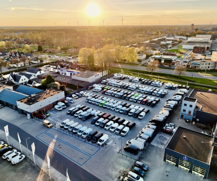 Luchtfoto van een groot autoterrein met meer dan 700+ bedrijfswagens en personenauto’s bij een Greven Automotive, met de zon laag aan de horizon.